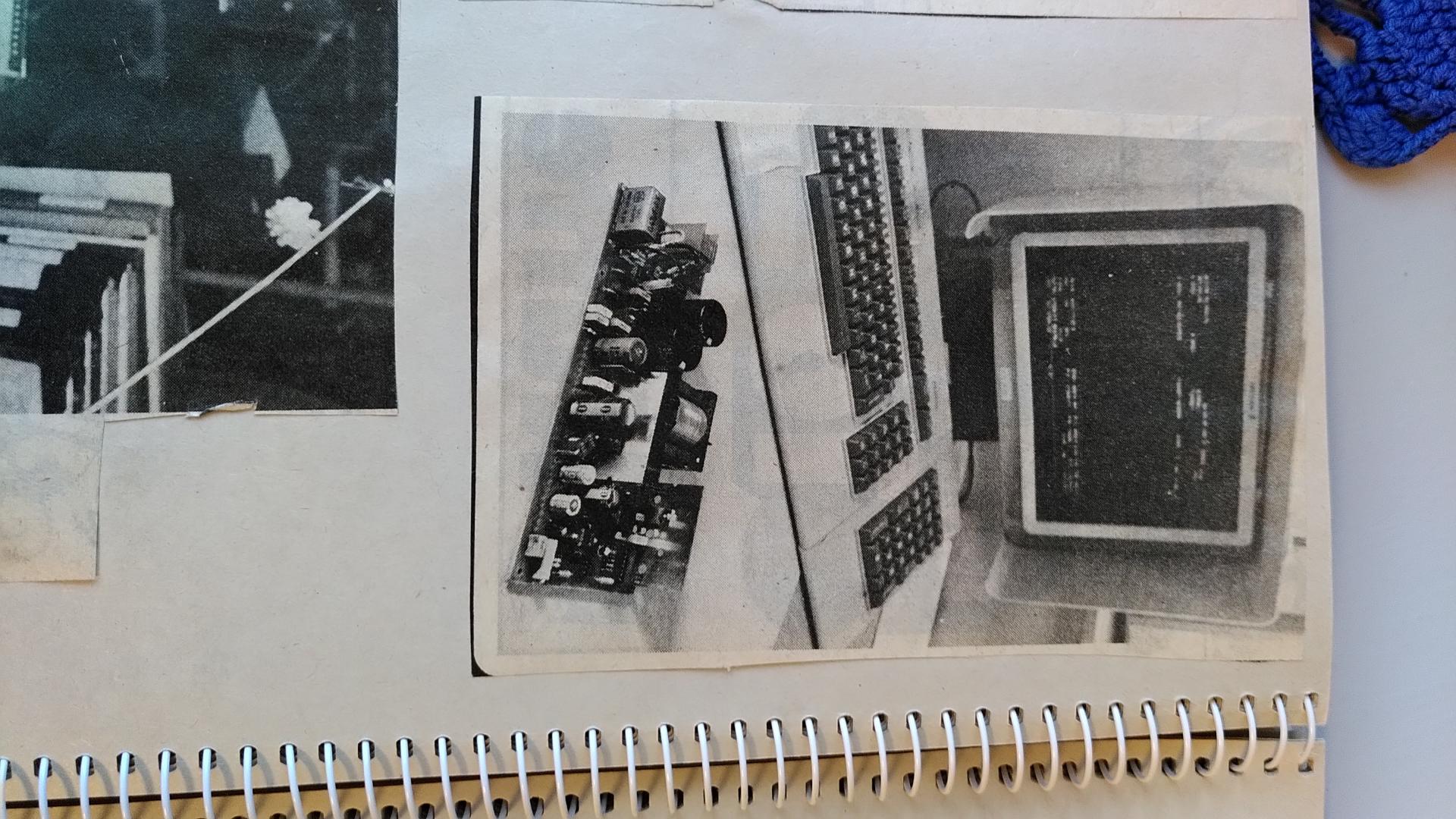 Black and white photo of a computer terminal display and keyboard. In front of it is an older type of a circuit board