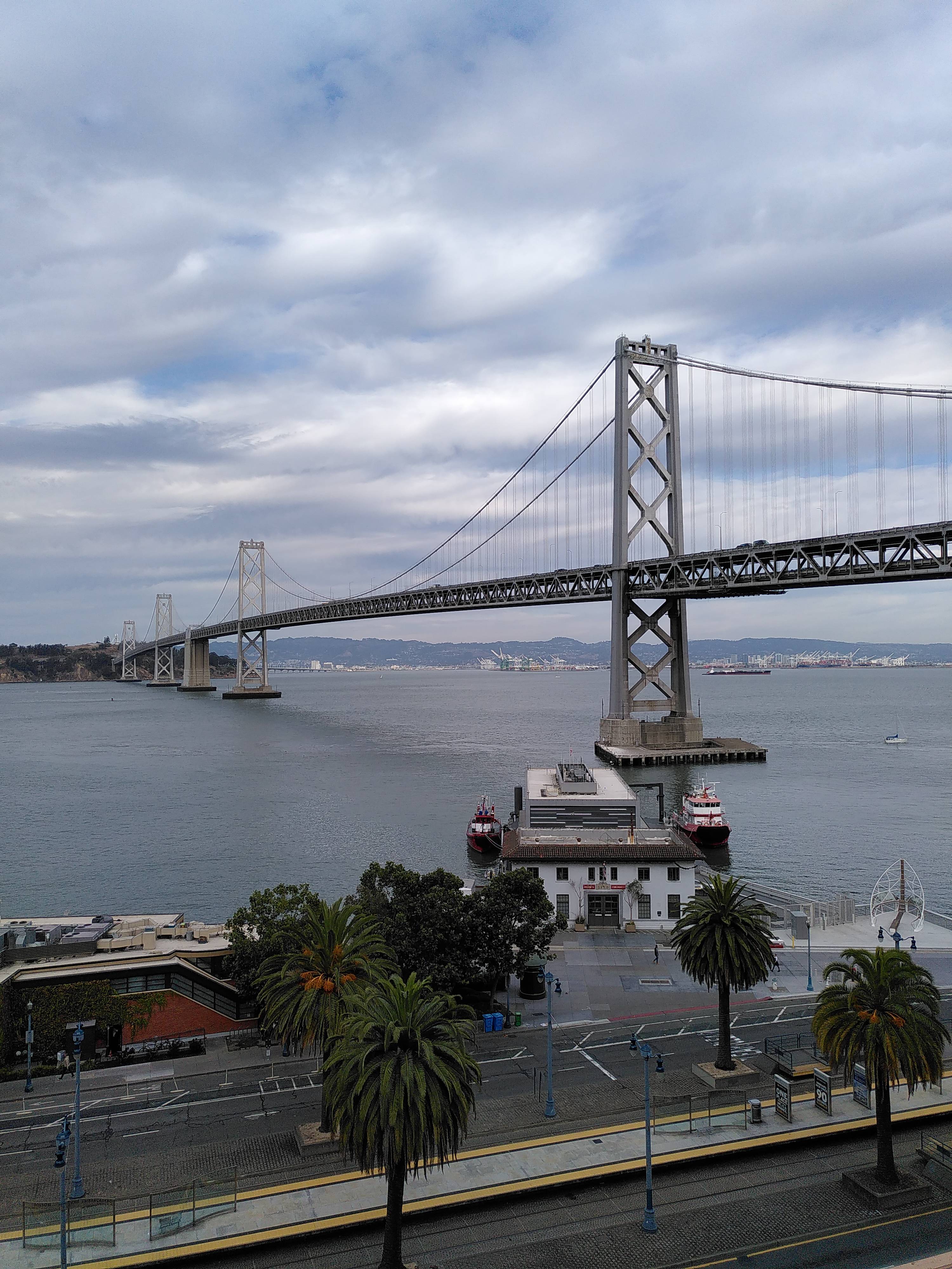 View of the Bay Bridge and a lot of water, as seen from a terrace high above street level.