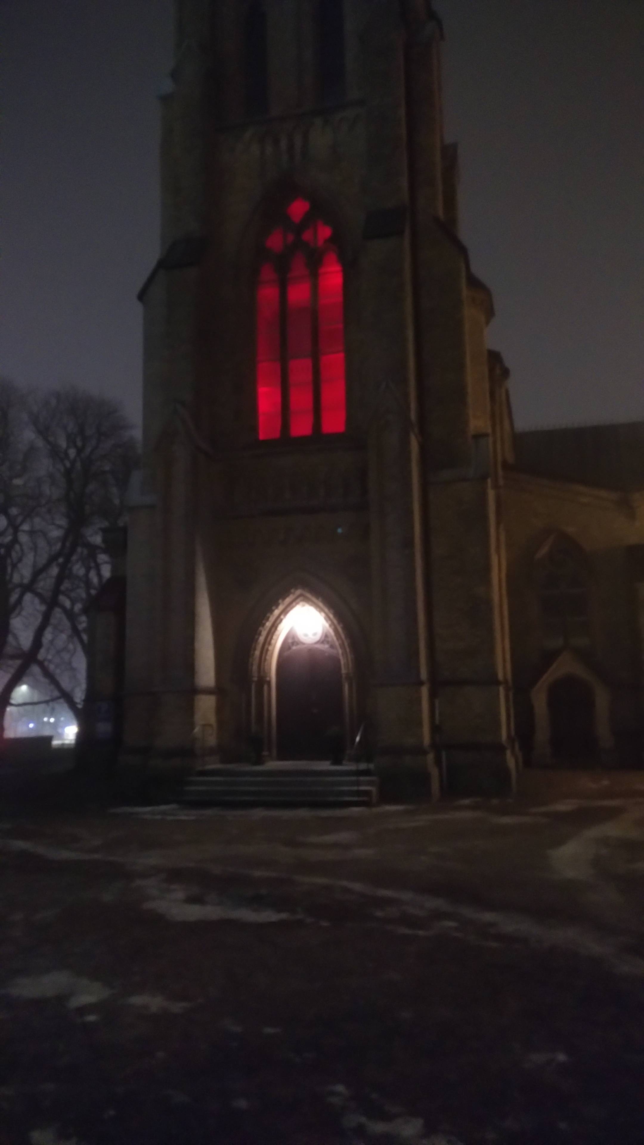 Part of the front of new-gothic church in the fog. The big windows are lighted up from within with red light.