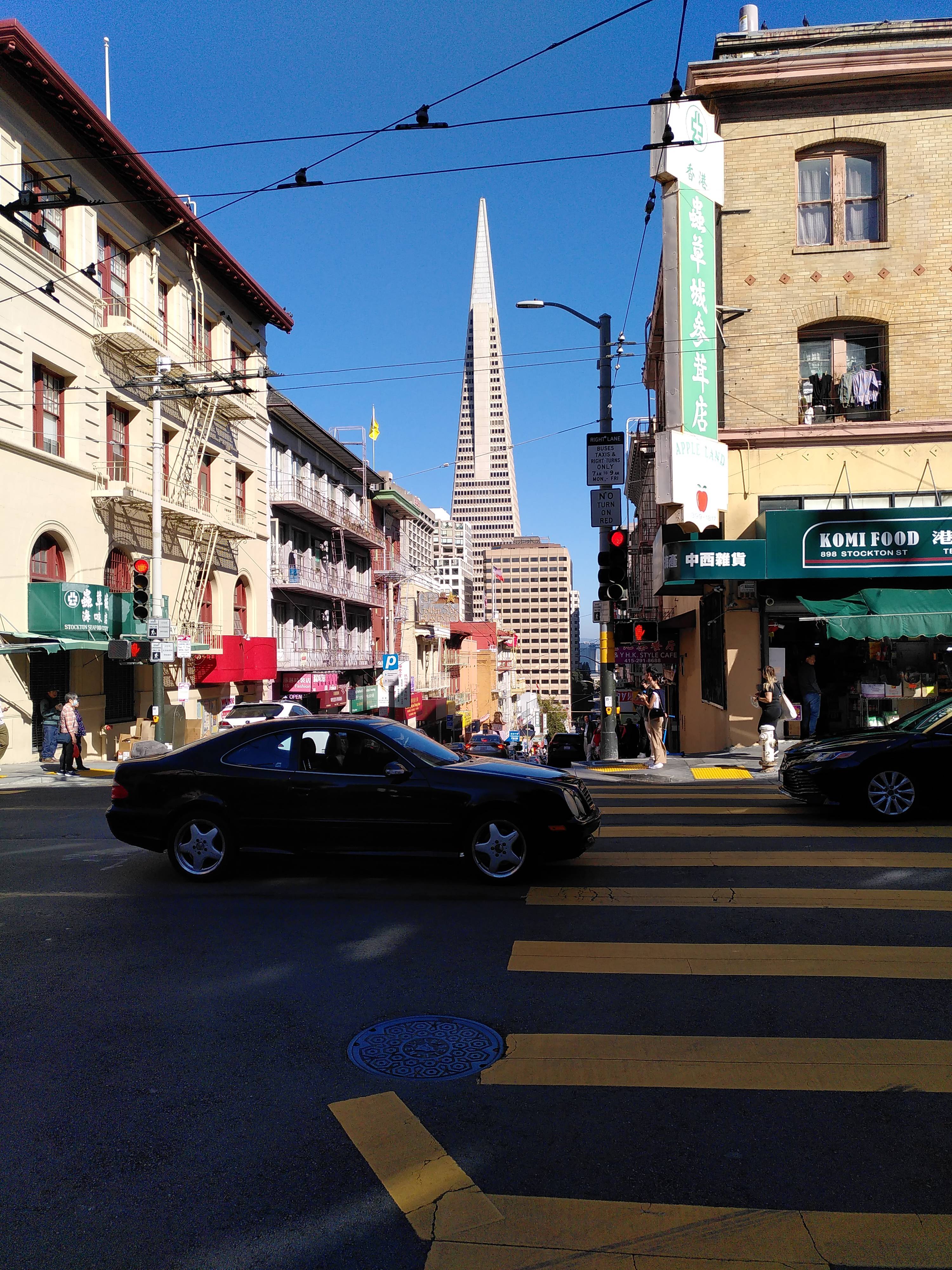 A crossing with low houses with chinese signs. In the background a famous SF scryscraper.