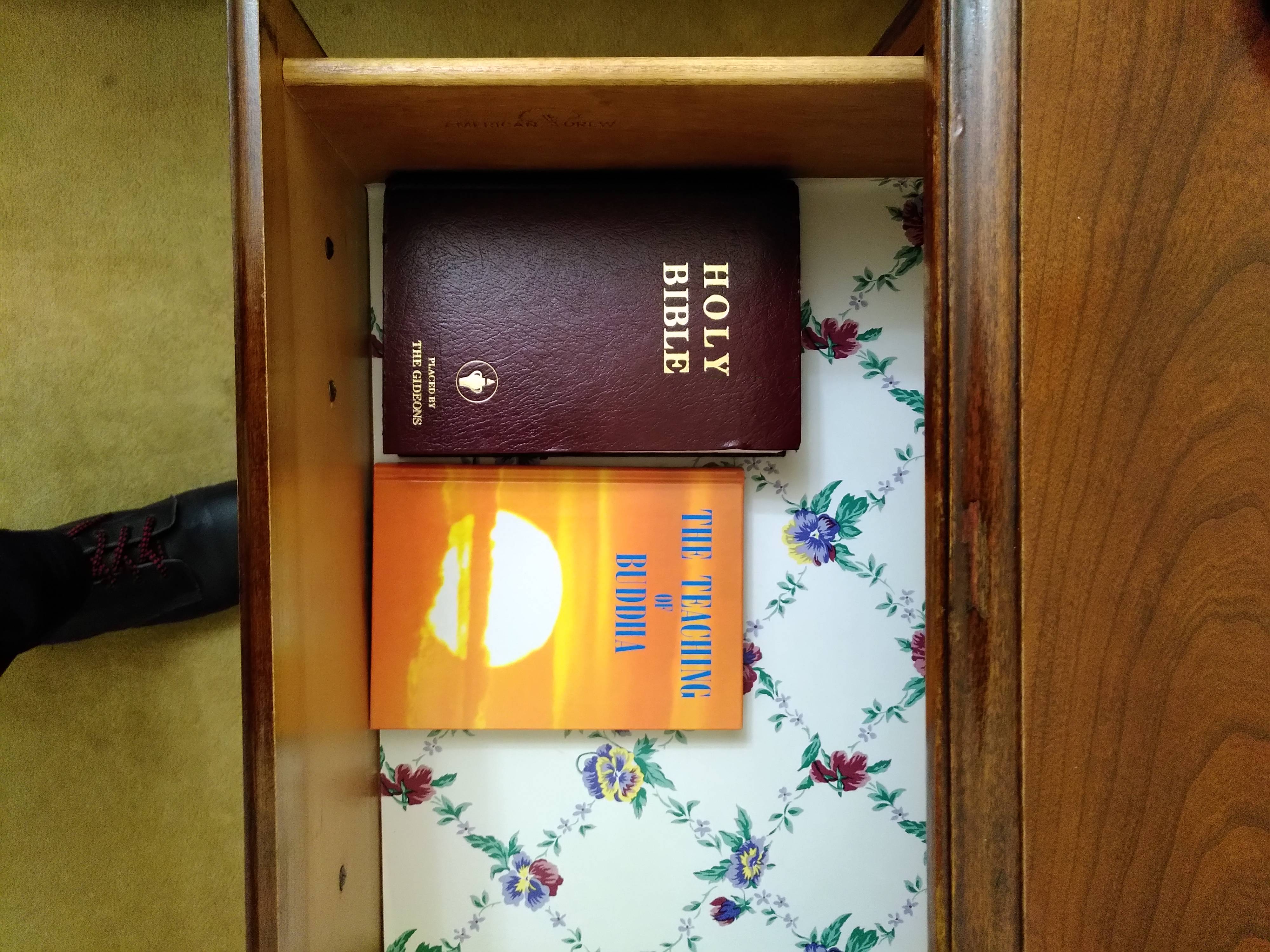 A drawer containing the bible and another book with the title "The teaching of the Buddha".