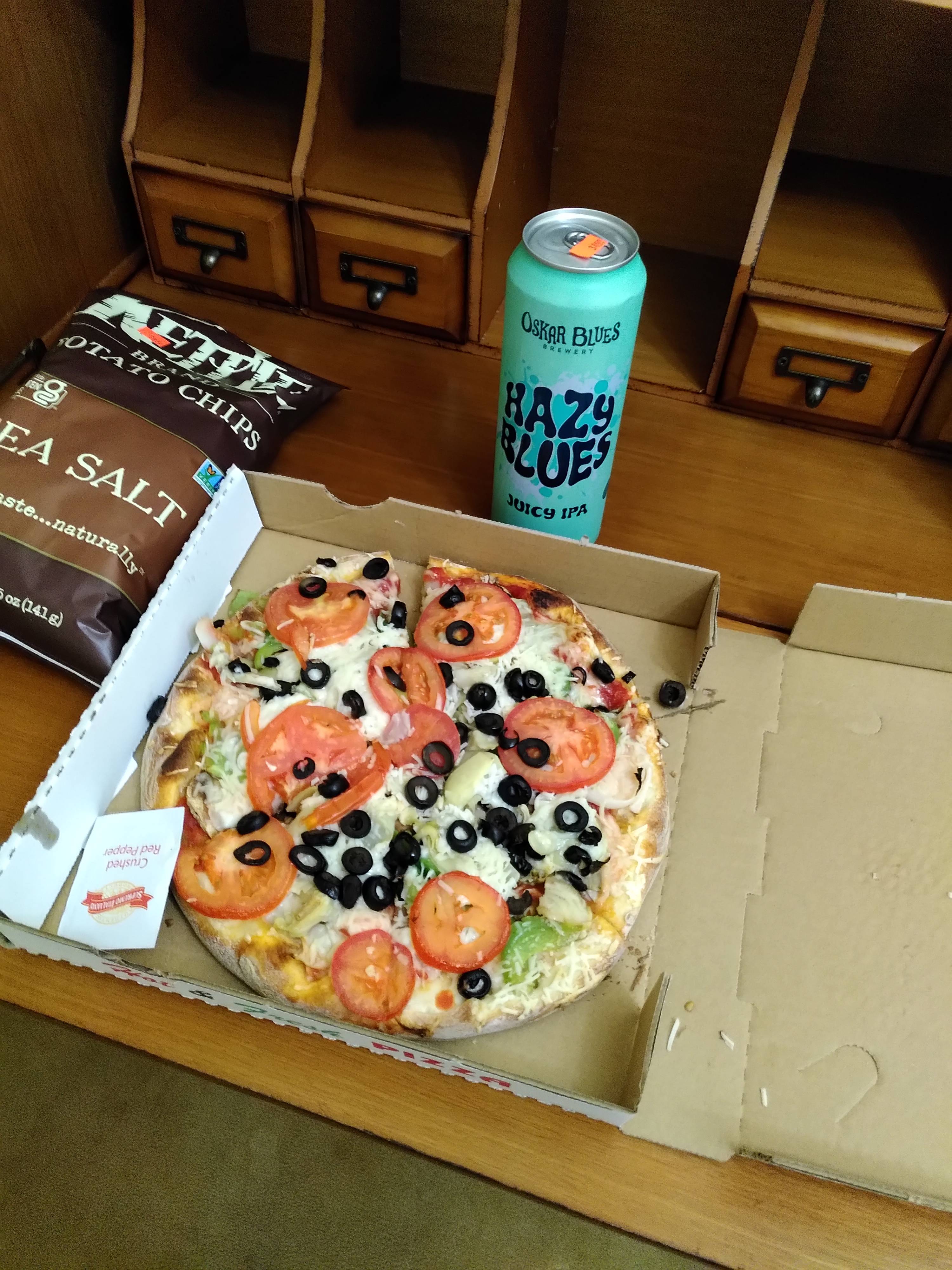 A small pizza, a beer can, and a bag of crisps on a victorian desk.