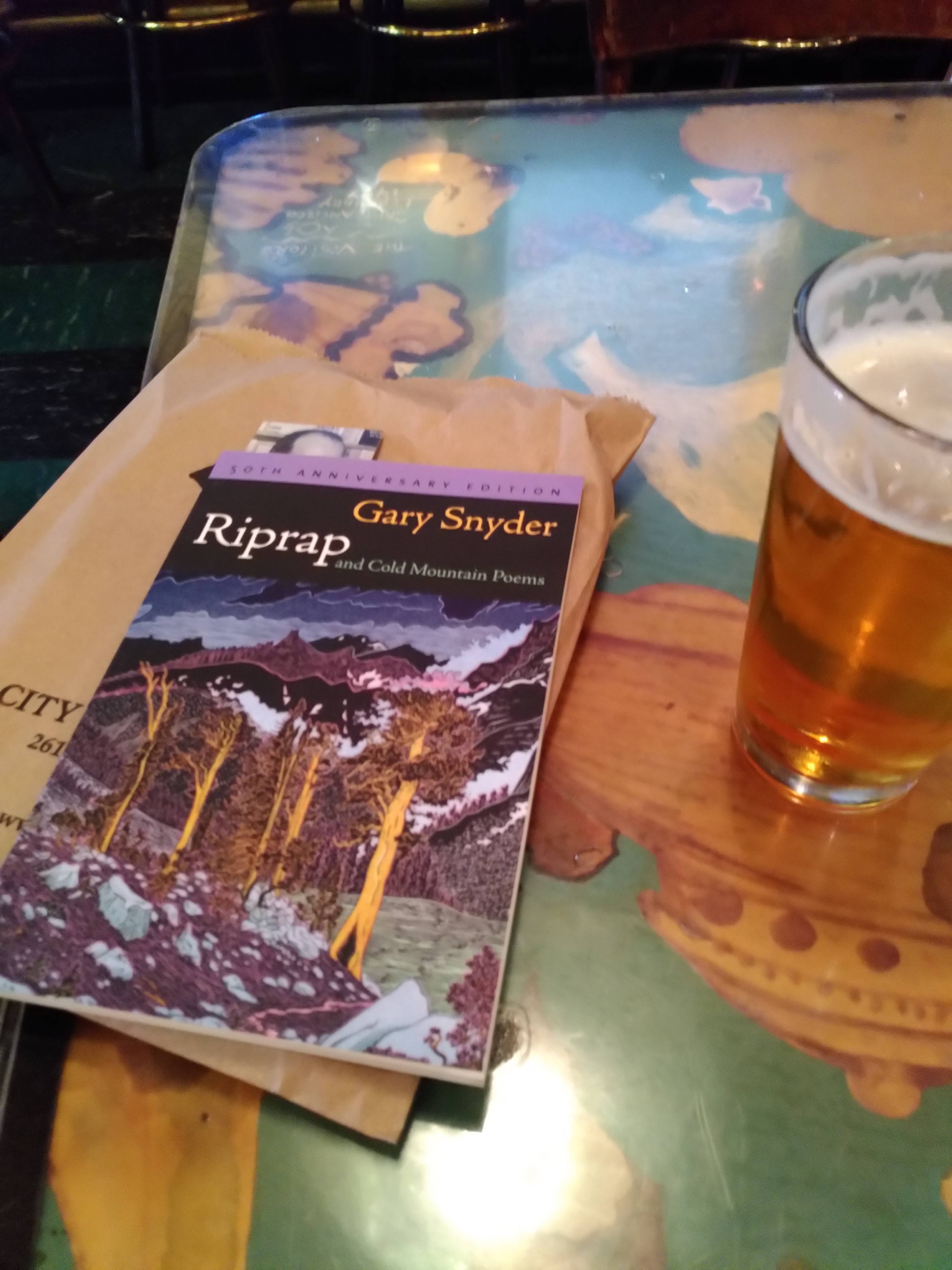 Gary Snyder's book "Riprap", which includes "Cold Mountain Poems" on a table with a glass of beer next to it.