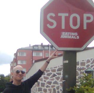 Picture of MC pointing to a STOP traffic sign where someone has added "eating animals".