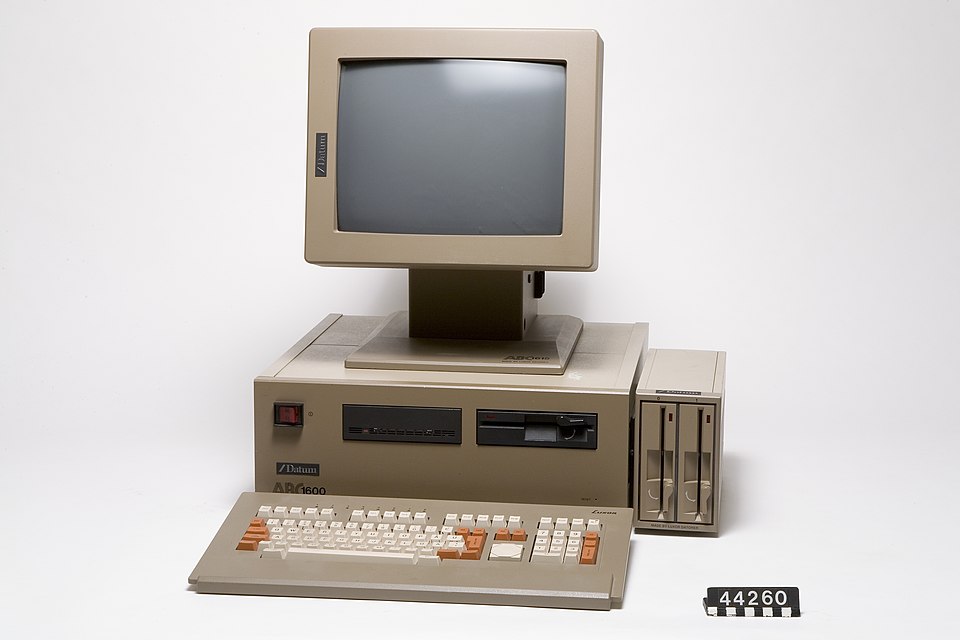 Museum setting, very white background: Brown, very high computer, with a large screen on a stand on top of it. In front a complicated keyboard, beside it an extra set of disk drives.