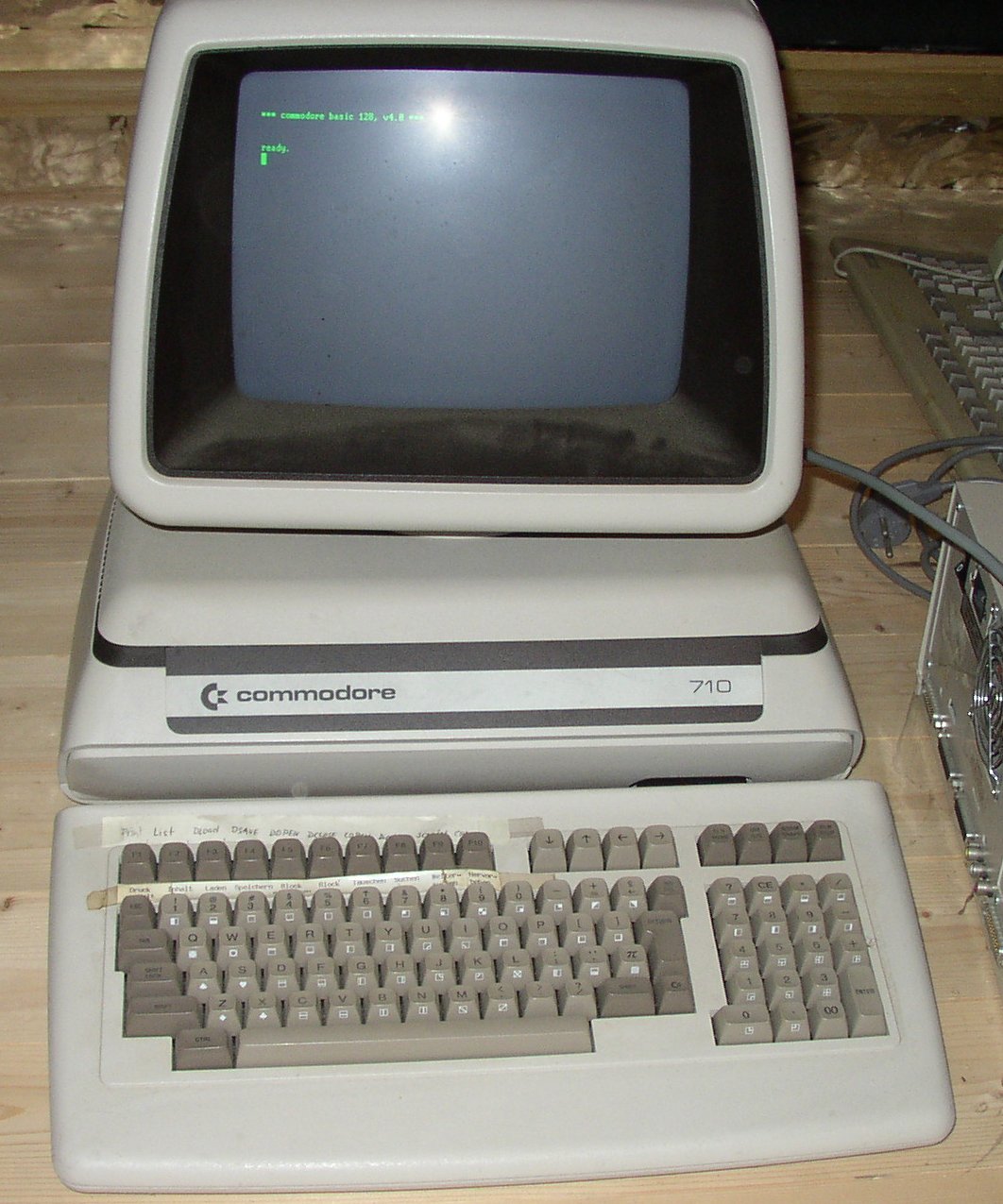 Porsche 911-like computer shell and monitor with a detached, but very high keyboard in front. The screen is showing some green characters saying that a version of BASIC is ready.
