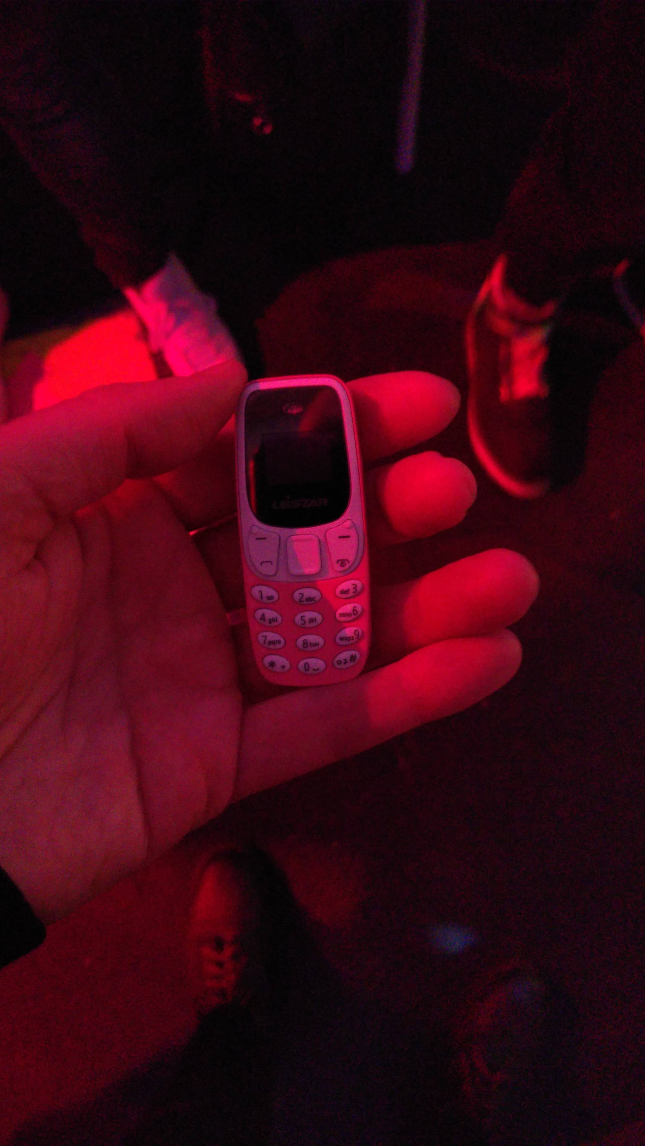 Very tiny phone in my hand, perhaps the size of my little finger. In the background the floor and some shoes.